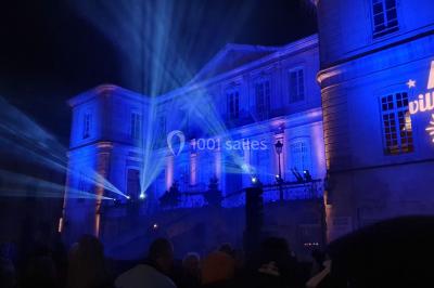 Salle avec éclairage de scène coloré, piste de danse illuminée, tables sur les côtés et matériel audio en arrière-plan.