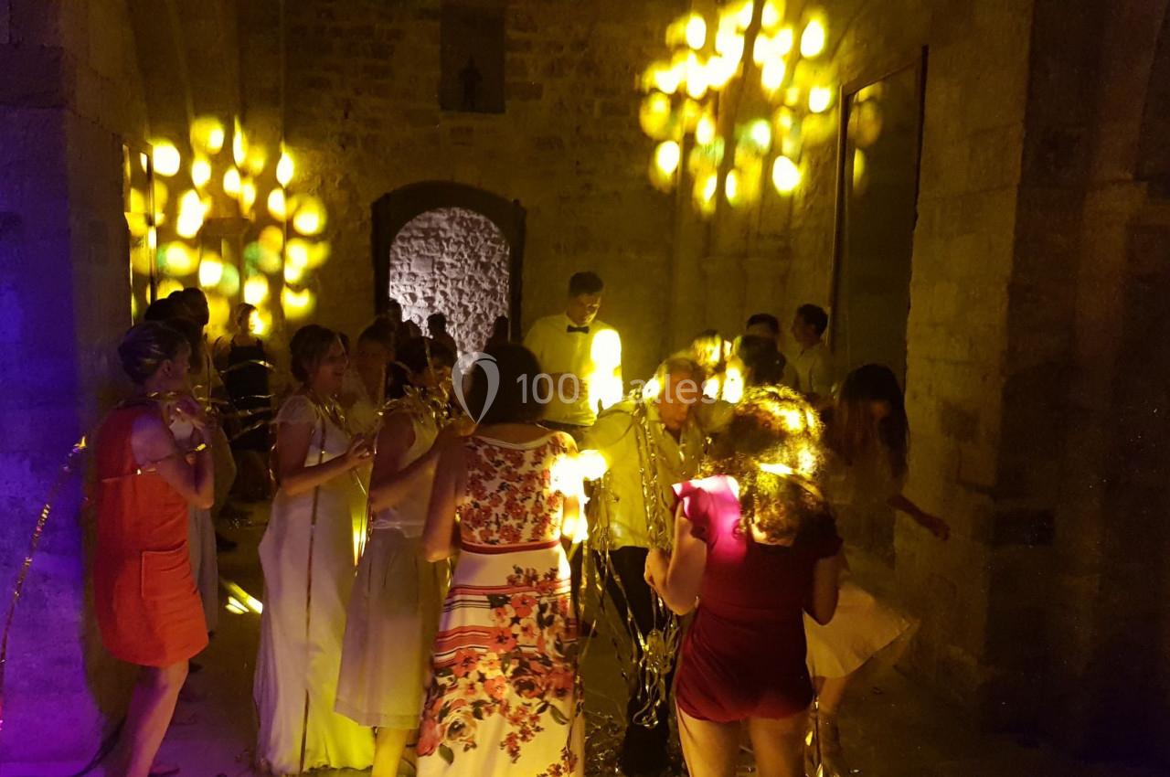 Groupe de personnes dans une salle en pierre faiblement éclairée, avec des lumières jaunes projetées sur les murs.