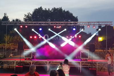 Salle avec éclairage de scène coloré, piste de danse illuminée, tables sur les côtés et matériel audio en arrière-plan.