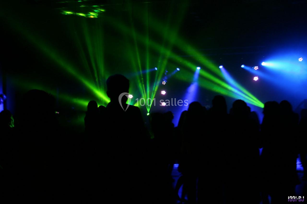 Personnes dansant dans une salle sombre illuminée par des faisceaux lumineux verts et bleus.