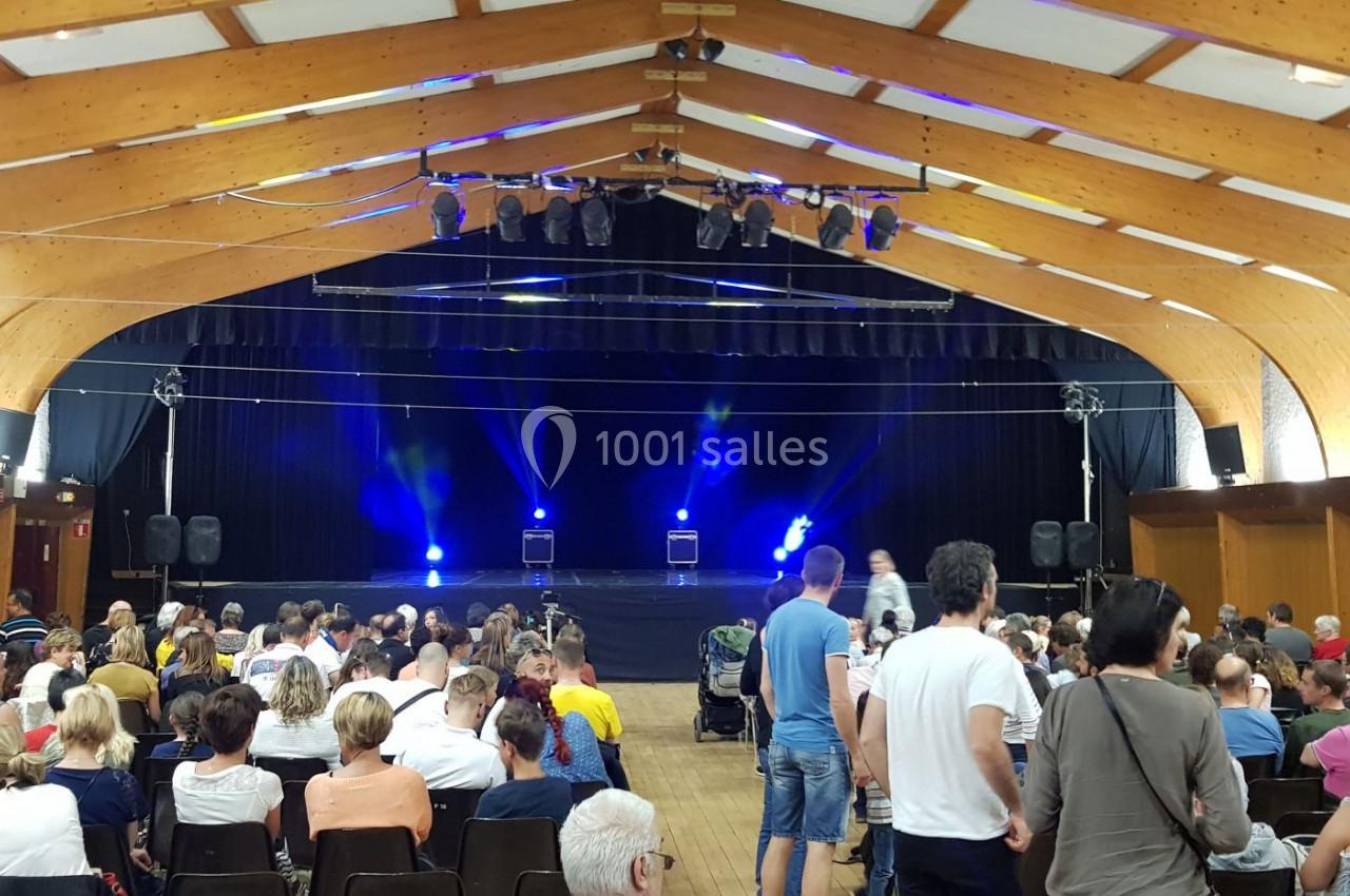 Salle de spectacle avec un public assis face à une scène éclairée par des projecteurs bleus.