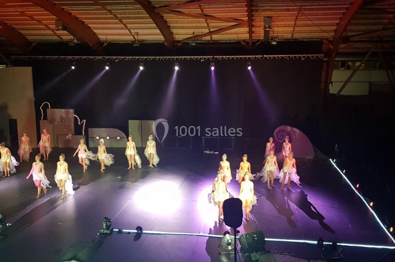Danseuses en costume évoluant sur une scène éclairée, entourée d'une structure en bois et d'effets lumineux.