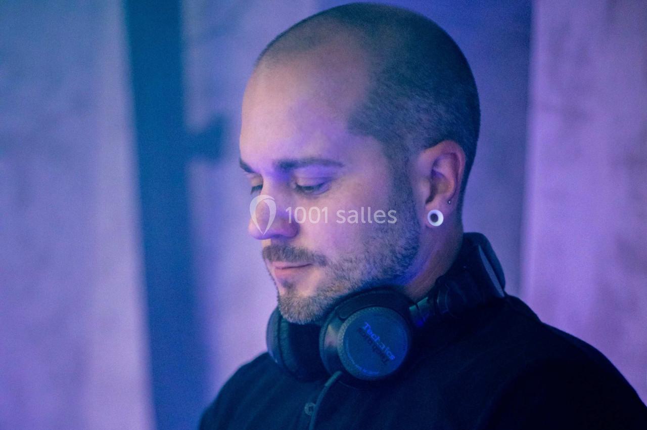 Homme chauve portant un casque audio autour du cou, éclairé par une lumière bleutée dans un environnement sombre.