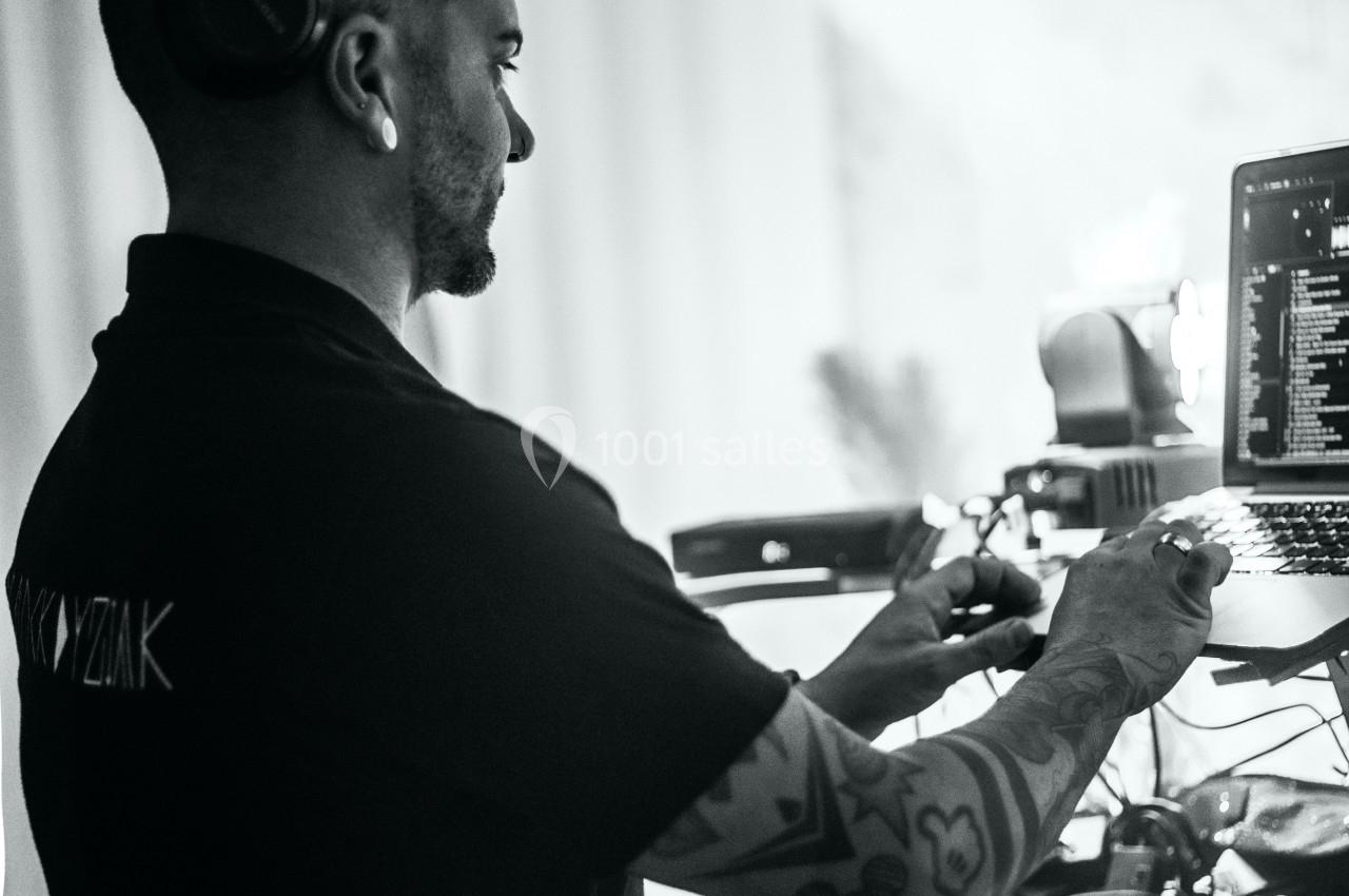 Un homme portant un casque ajuste des équipements audio près d'un ordinateur portable dans un environnement lumineux.