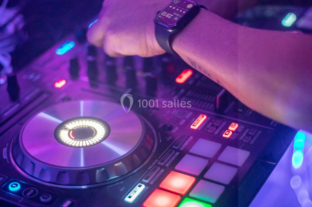 Main ajustant les commandes d'une table de mixage lumineuse dans une ambiance colorée.