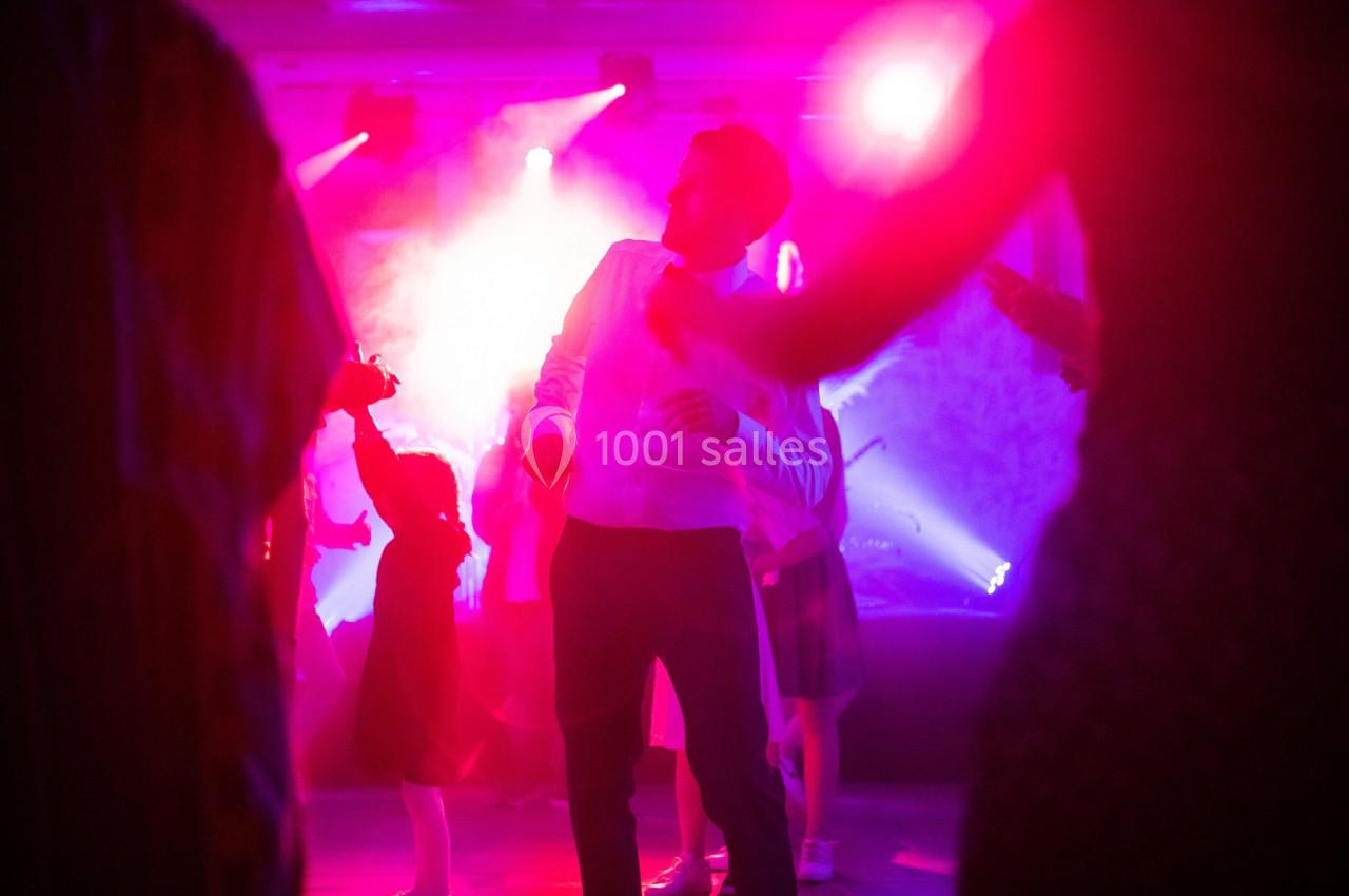 Un homme en chemise blanche danse au milieu d'une foule sous des lumières colorées dans une ambiance festive.