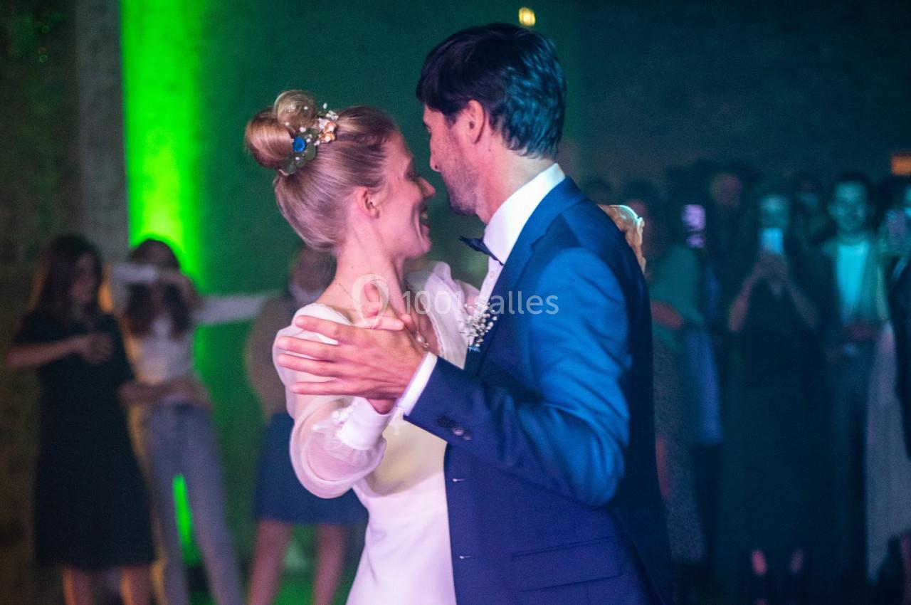 Un couple danse lors d'une réception, entouré d'invités dans une ambiance lumineuse tamisée.