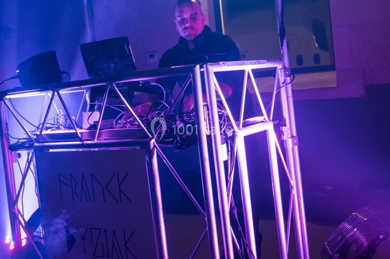 Un DJ mixant de la musique derrière une console éclairée par des lumières violettes dans une ambiance nocturne.