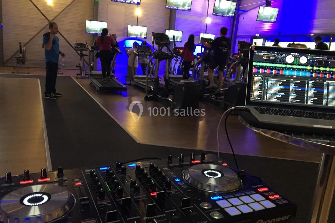 Salle de sport avec des personnes sur des tapis de course, éclairage bleu et table de mixage en premier plan.