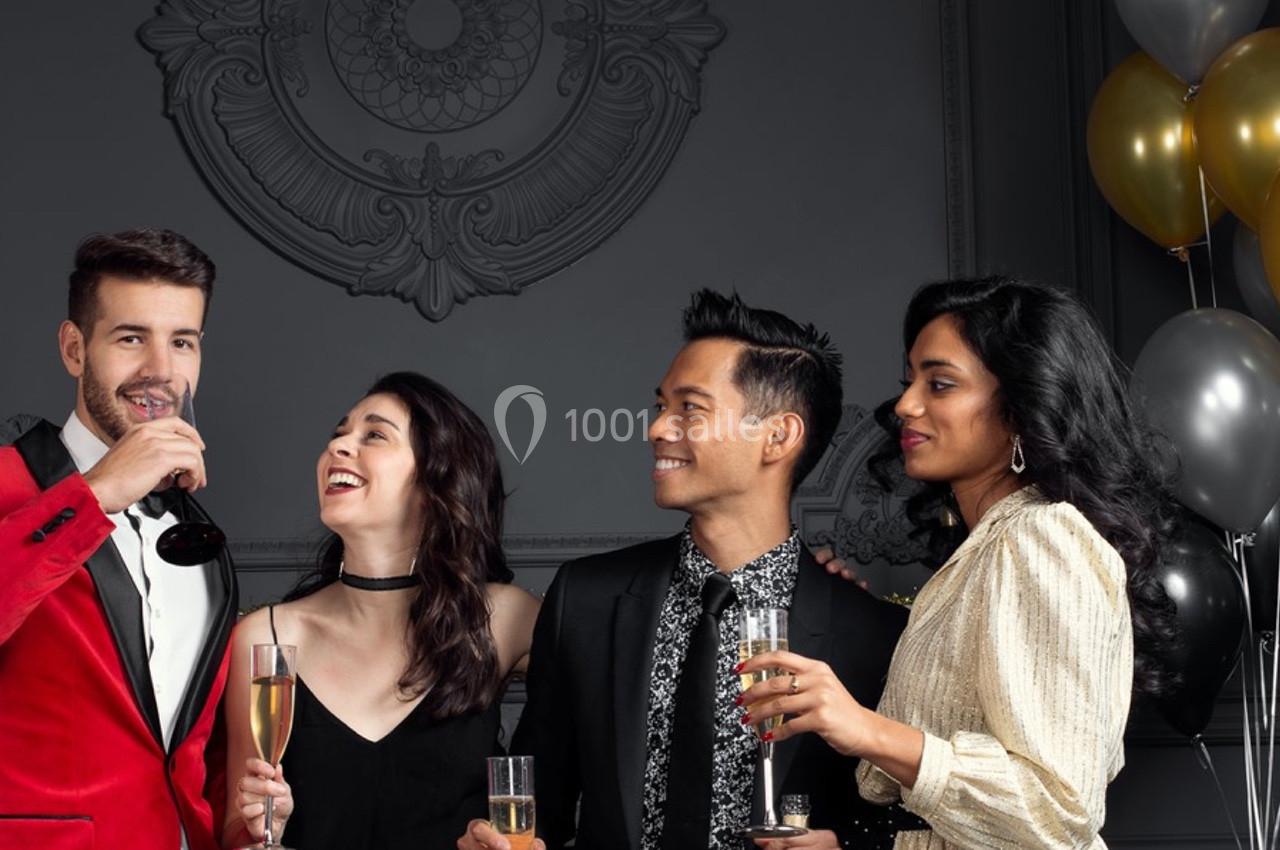 Quatre personnes élégamment vêtues discutent et trinquent avec des verres de champagne dans un décor raffiné.