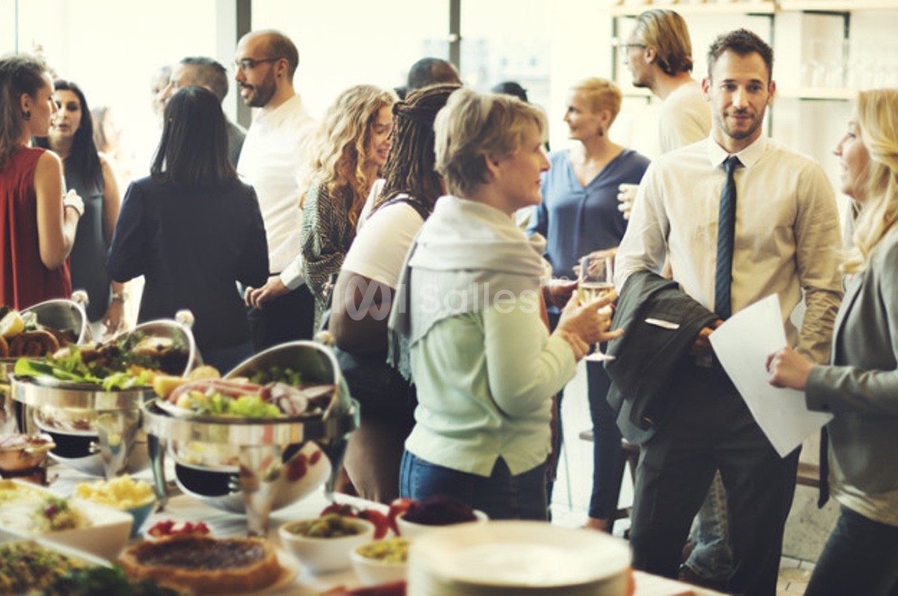 Des personnes discutent debout lors d'un événement avec un buffet de plats variés au premier plan.