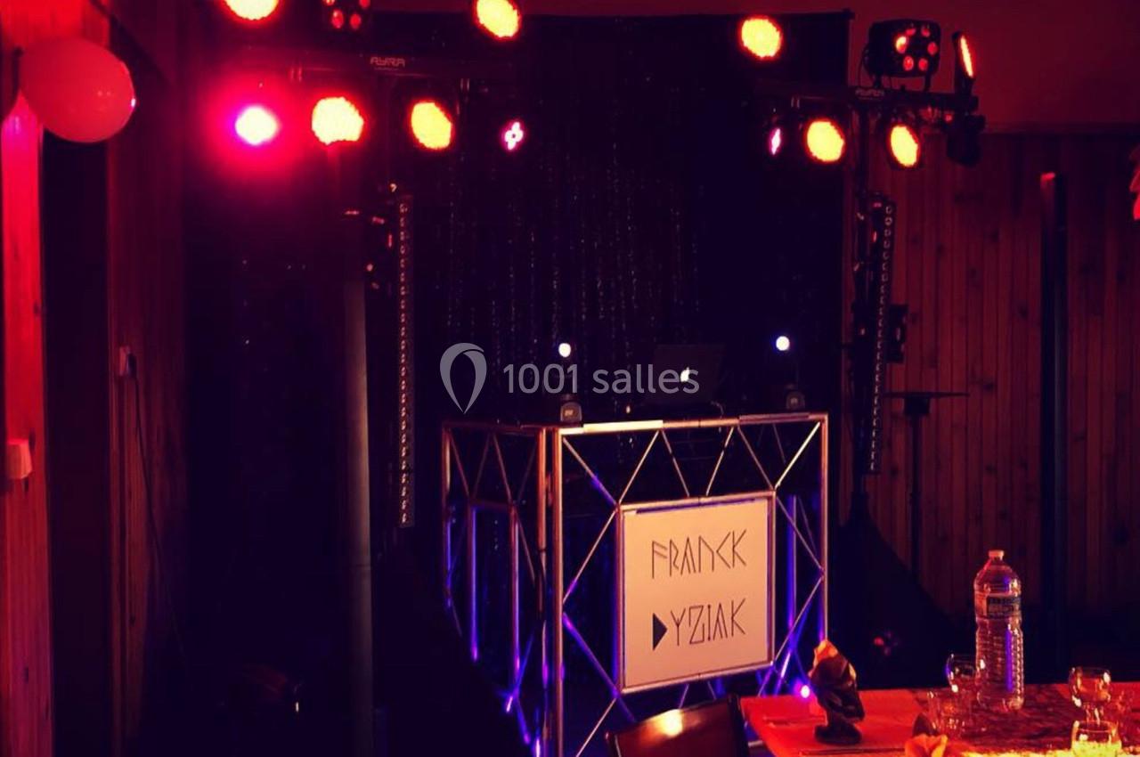Installation de DJ avec éclairage coloré et table de mixage dans une salle sombre aux murs en bois.