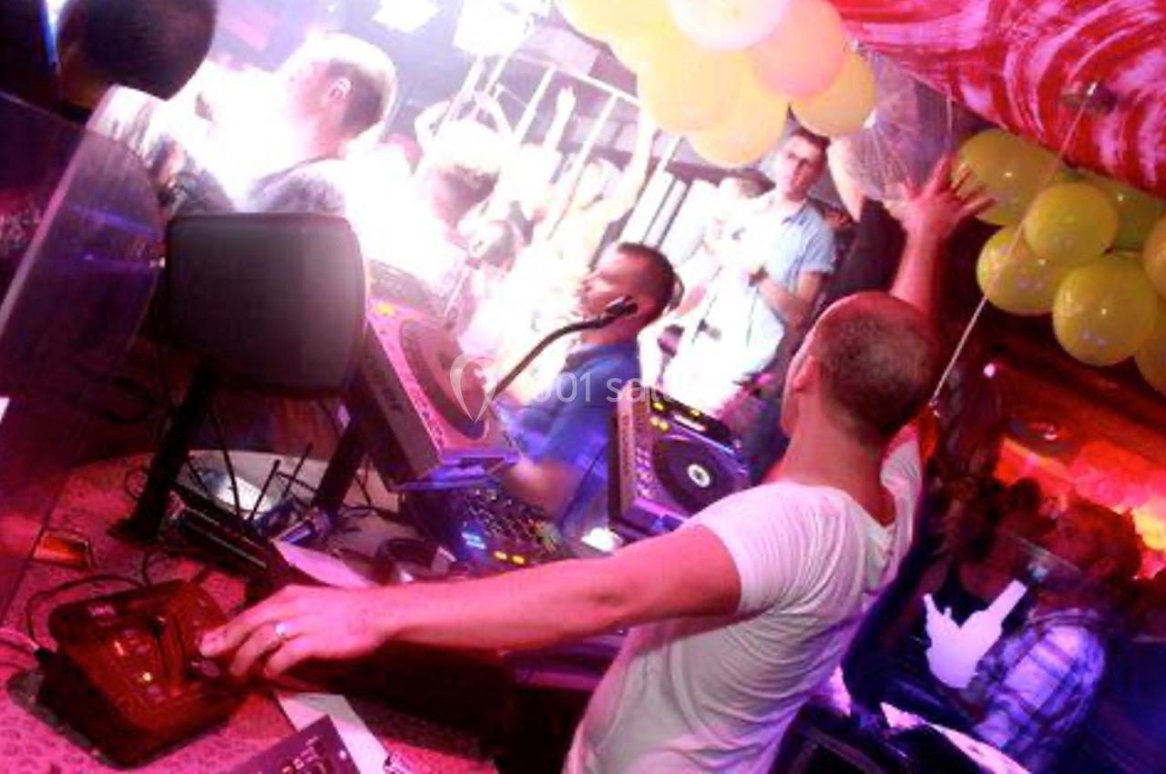 Un DJ mixe sur une scène éclairée, entouré de ballons jaunes et d'une foule dans une ambiance festive.