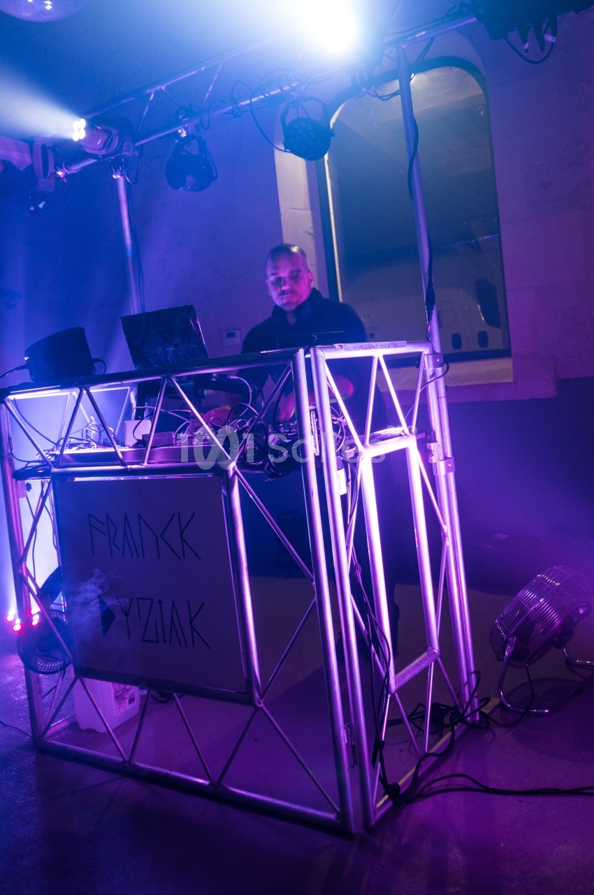 Un DJ mixant sur une scène éclairée de lumières violettes dans un environnement intérieur.