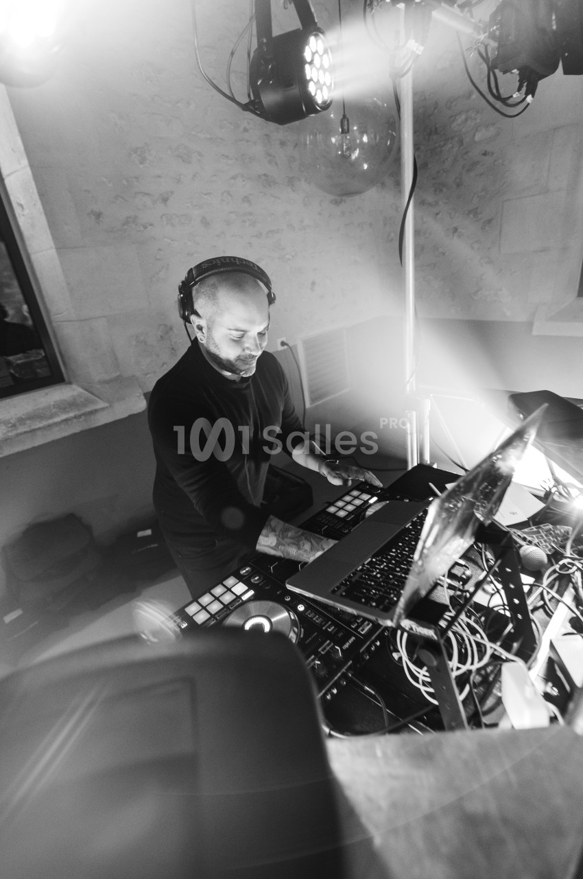 Un DJ mixant de la musique sur une table de mixage entourée d'équipements électroniques dans une ambiance lumineuse.