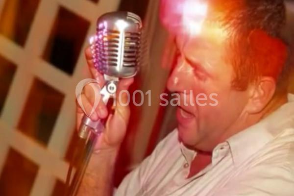 Homme chantant dans un microphone rétro, éclairé par des lumières colorées en arrière-plan.