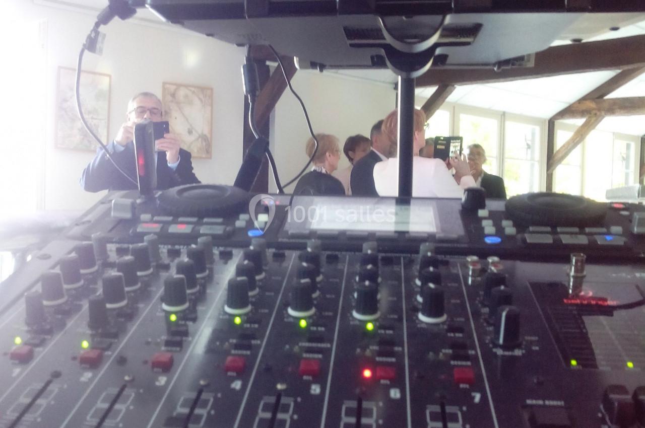 Table de mixage audio en gros plan avec un écran de contrôle vidéo en arrière-plan, dans une salle lumineuse.