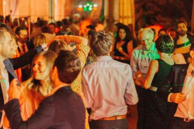 Des personnes dansent et lèvent les bras dans une ambiance festive, éclairée par des lumières colorées.