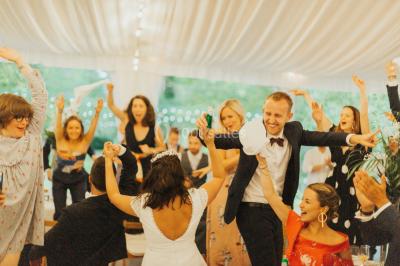 Des personnes dansent et lèvent les bras dans une ambiance festive, éclairée par des lumières colorées.