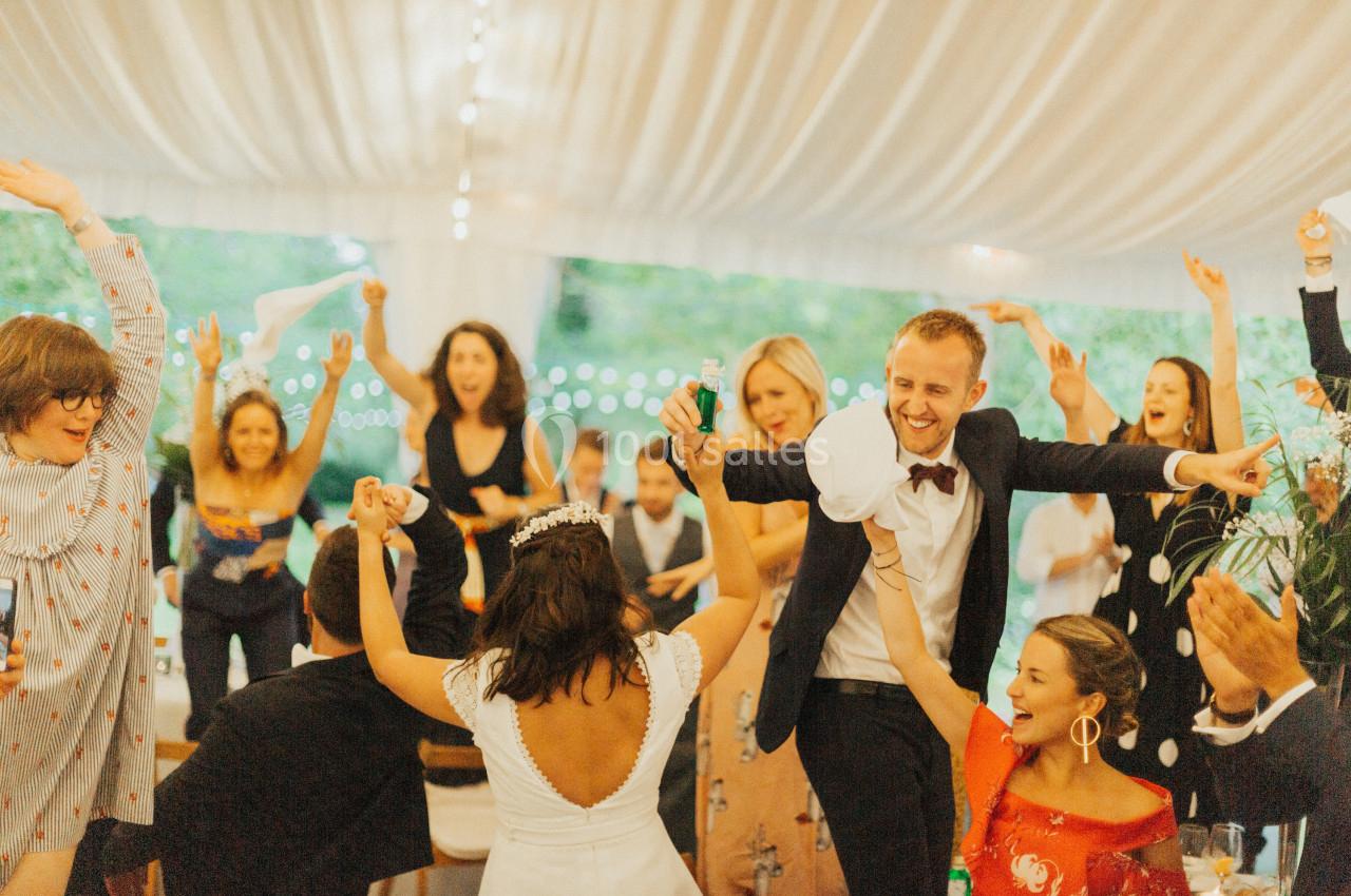 Des invités dansent et célèbrent sous une tente décorée, avec une mariée et un marié au centre de l'attention.