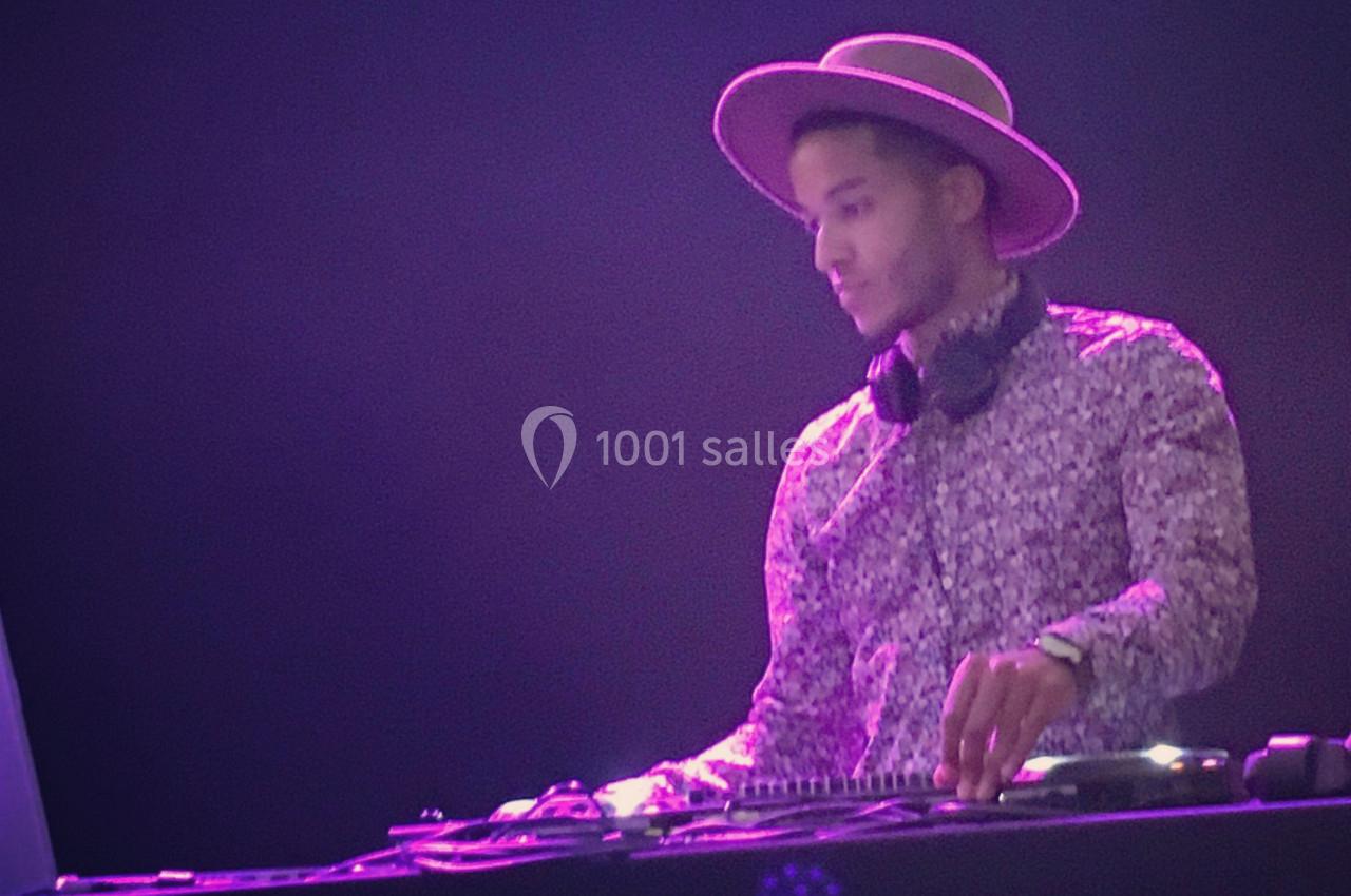 Un DJ portant un chapeau et un casque mixe de la musique sur une table de mixage dans une ambiance lumineuse tamisée.