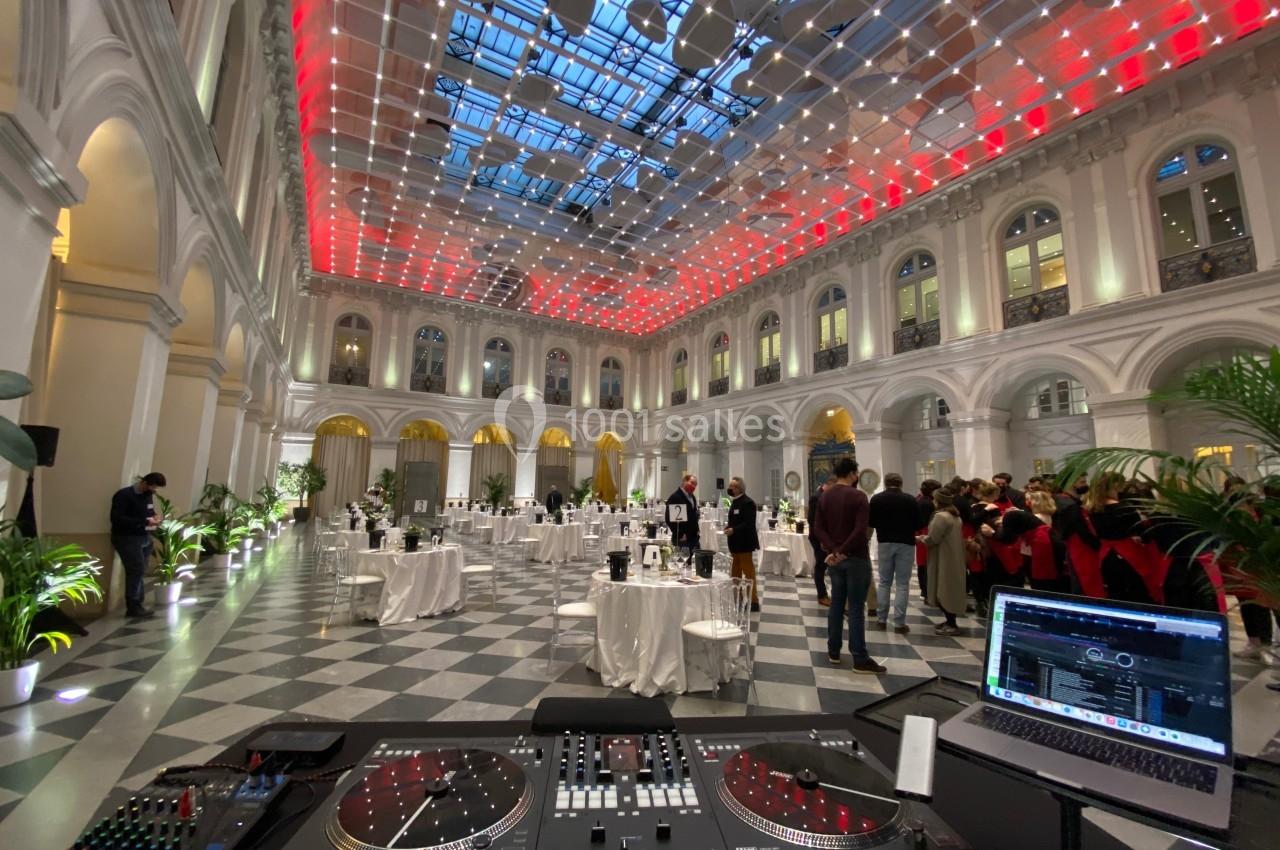 Salle de réception élégante avec plafond lumineux, tables dressées et équipement de DJ au premier plan.