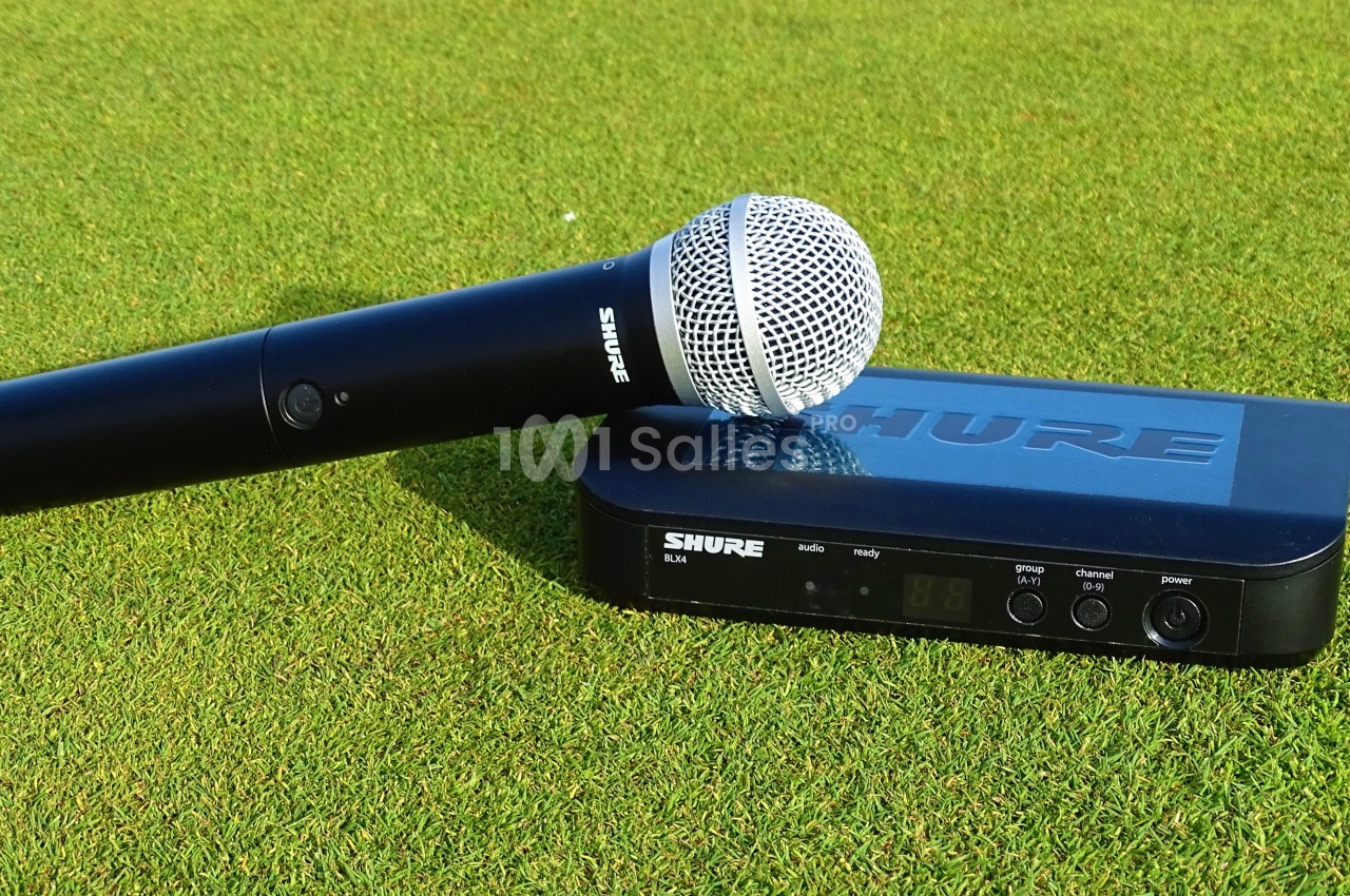 Microphone sans fil noir et récepteur posés sur une pelouse verte.