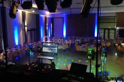 Salle décorée avec un sapin de Noël, éclairages colorés au sol et matériel de DJ installé sur une estrade.