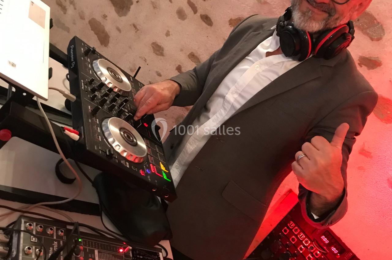 Un homme souriant en costume mixe de la musique sur une table de mixage dans un espace intérieur en pierre.