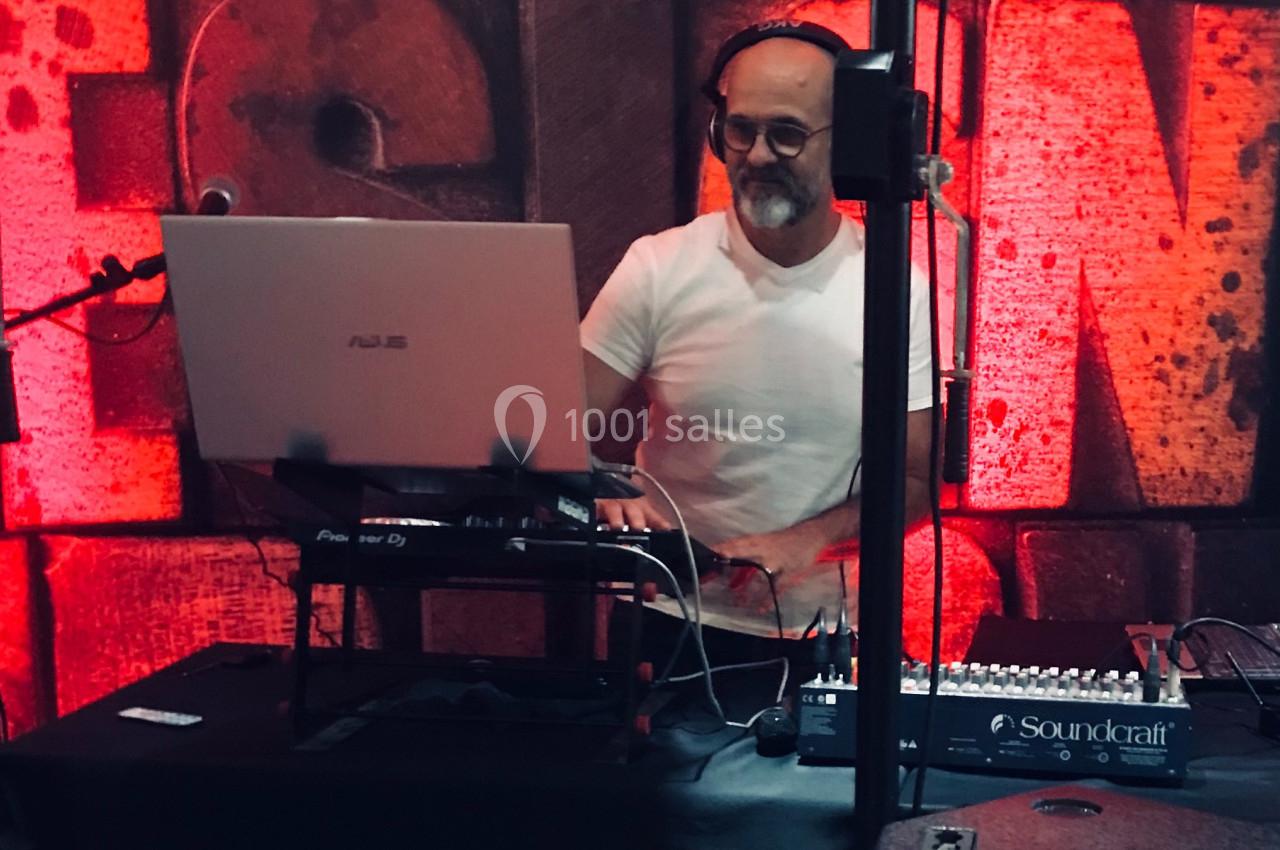 Un homme avec un casque audio mixe de la musique sur un ordinateur portable devant un mur rouge texturé.