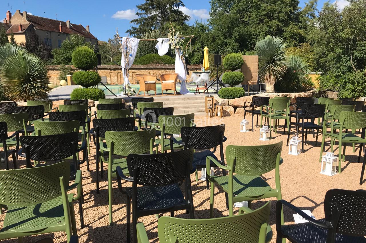 Chaises disposées en rangées face à une scène extérieure décorée, entourée de végétation et de bâtiments en arrière-plan.