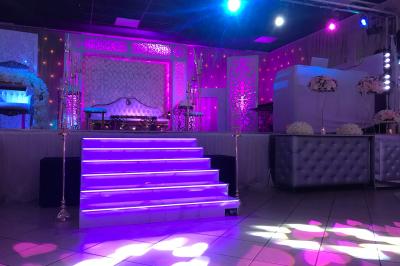 Salle décorée avec un sapin de Noël, éclairages colorés au sol et matériel de DJ installé sur une estrade.