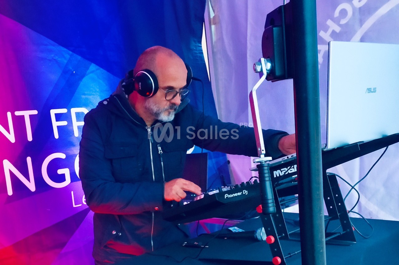 Un DJ portant un casque mixe de la musique sur une table de mixage dans un environnement extérieur couvert.