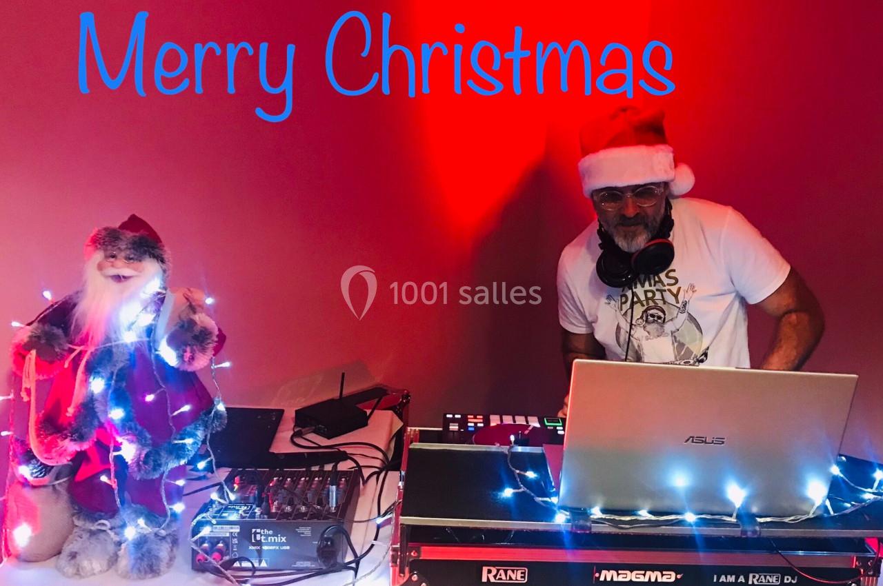 Un DJ portant un bonnet de Noël mixe de la musique à côté d'une décoration lumineuse de Père Noël.
