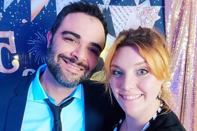 Un homme et une femme sourient devant un fond décoré de feuillage et de rideaux blancs.