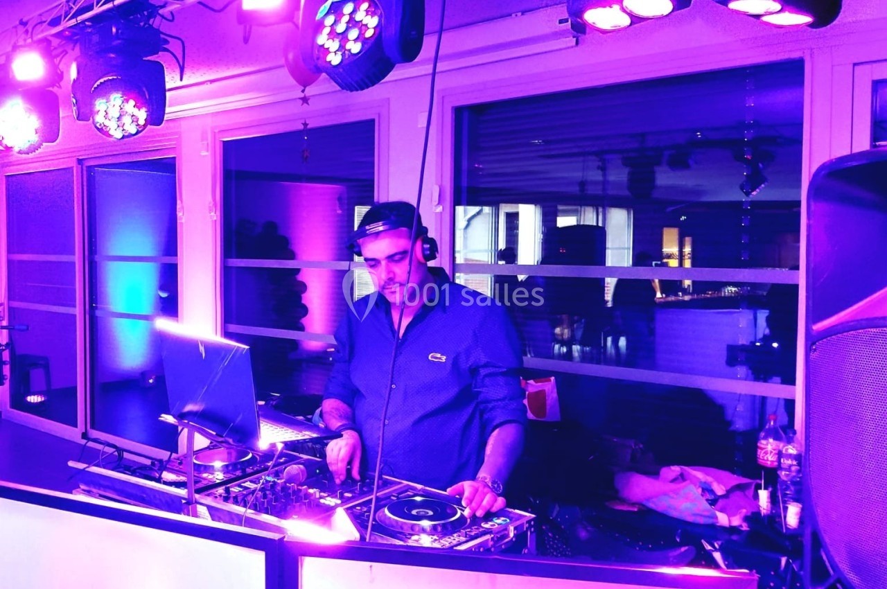 Un DJ mixant de la musique sur une table de mixage, entouré de lumières violettes dans une salle.