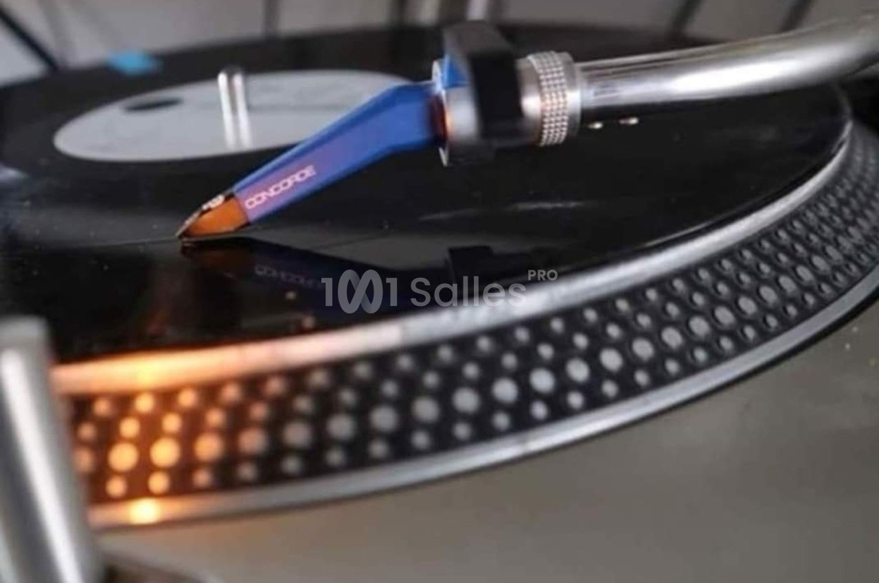 Bras de lecture bleu d'une platine vinyle en train de lire un disque noir, avec un éclairage chaud.