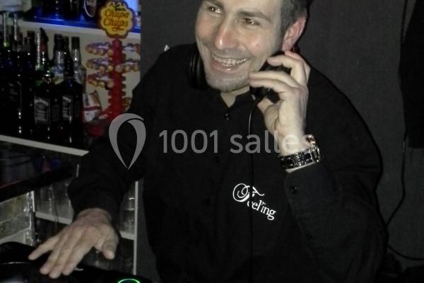 Homme souriant portant un casque audio, manipulant une table de mixage dans un environnement de bar.