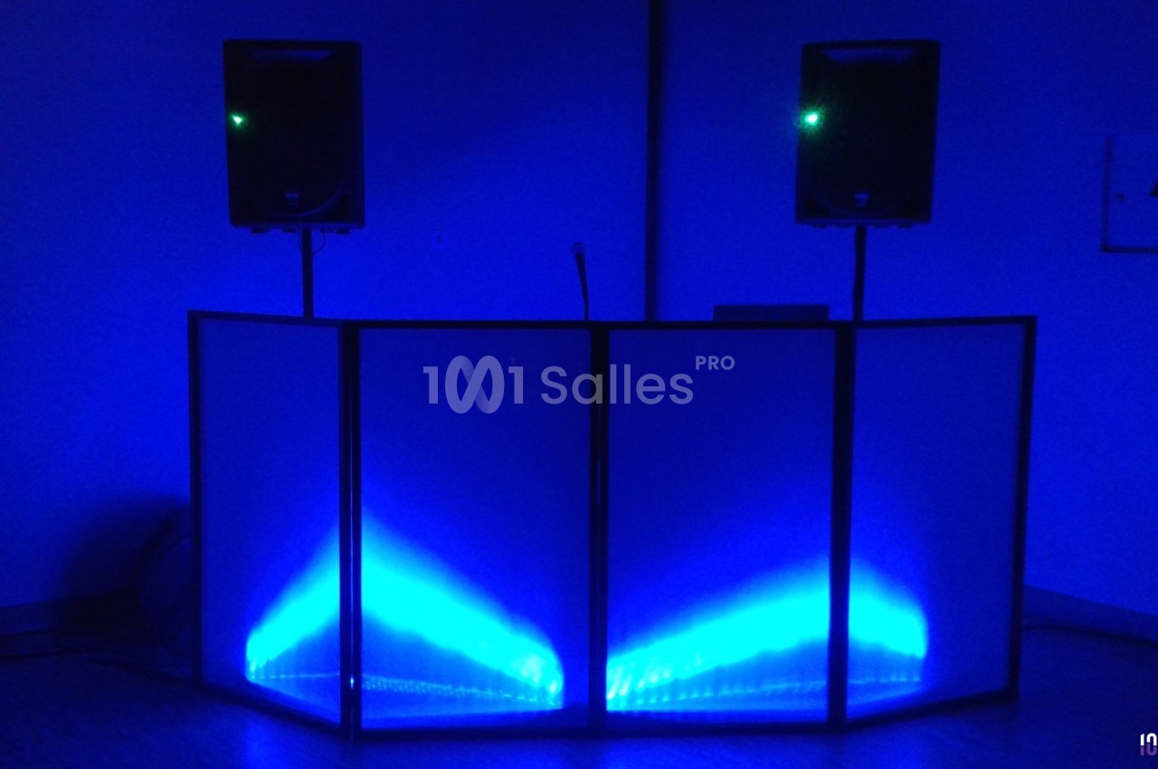 Console de DJ éclairée par des lumières bleues, entourée de deux enceintes sur pieds dans une pièce sombre.