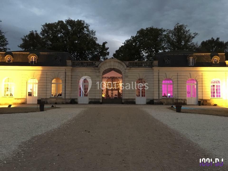 Façade d'un bâtiment historique éclairé par des lumières colorées, entouré d'arbres au crépuscule.
