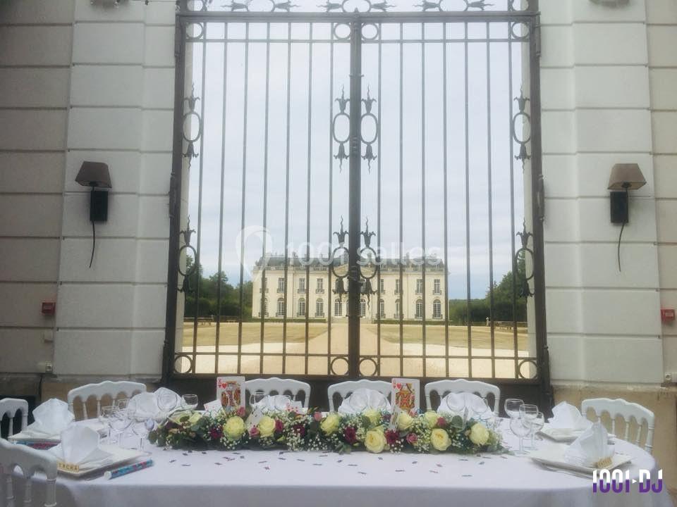 Table dressée avec des fleurs et vaisselle élégante devant une grille en fer forgé, avec un château en arrière-plan.
