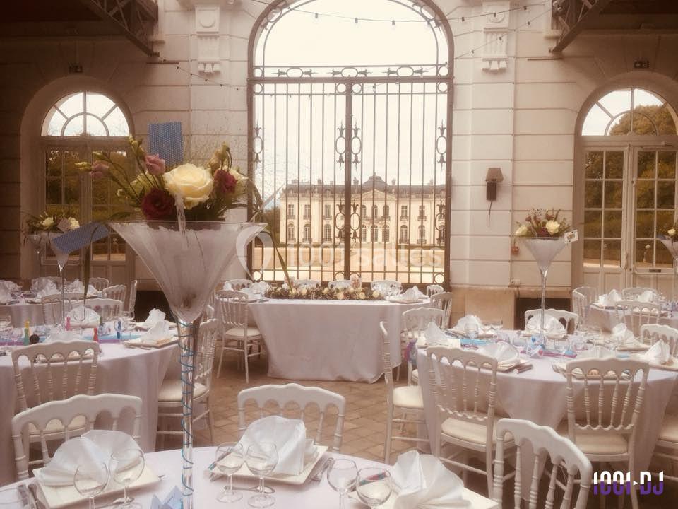 Tables élégamment dressées pour un événement dans une cour avec vue sur un bâtiment historique à travers une grille.