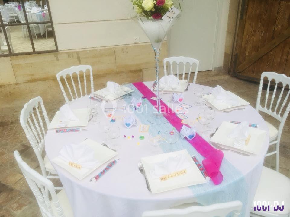 Table ronde décorée pour un événement, avec nappes blanches, chemin de table rose et bleu, et vaisselle élégante.