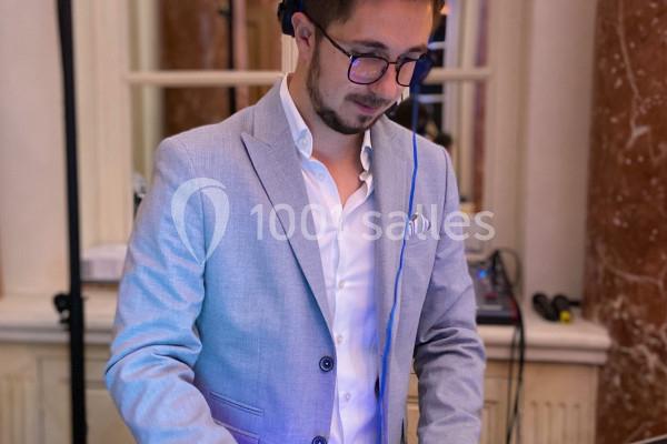 Un homme portant un costume clair mixe de la musique sur une table de mixage dans un intérieur élégant.