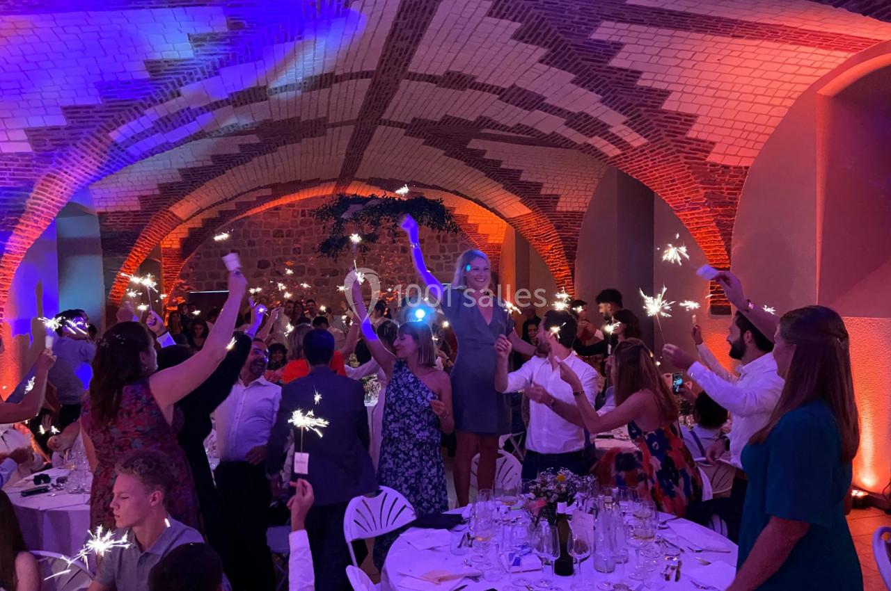 Des invités célèbrent dans une salle voûtée illuminée, tenant des cierges magiques allumés.