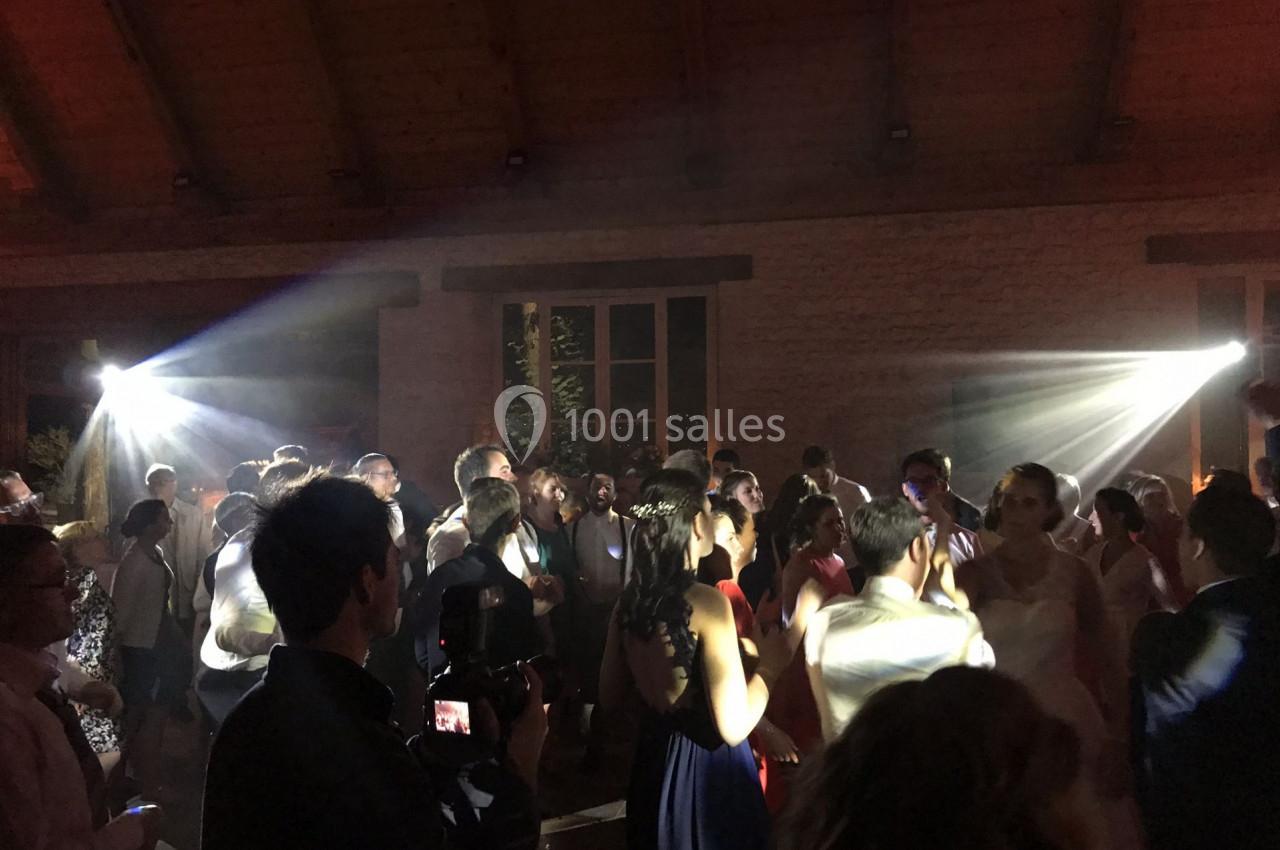 Des personnes dansent dans une salle faiblement éclairée avec des jeux de lumière et un photographe au premier plan.