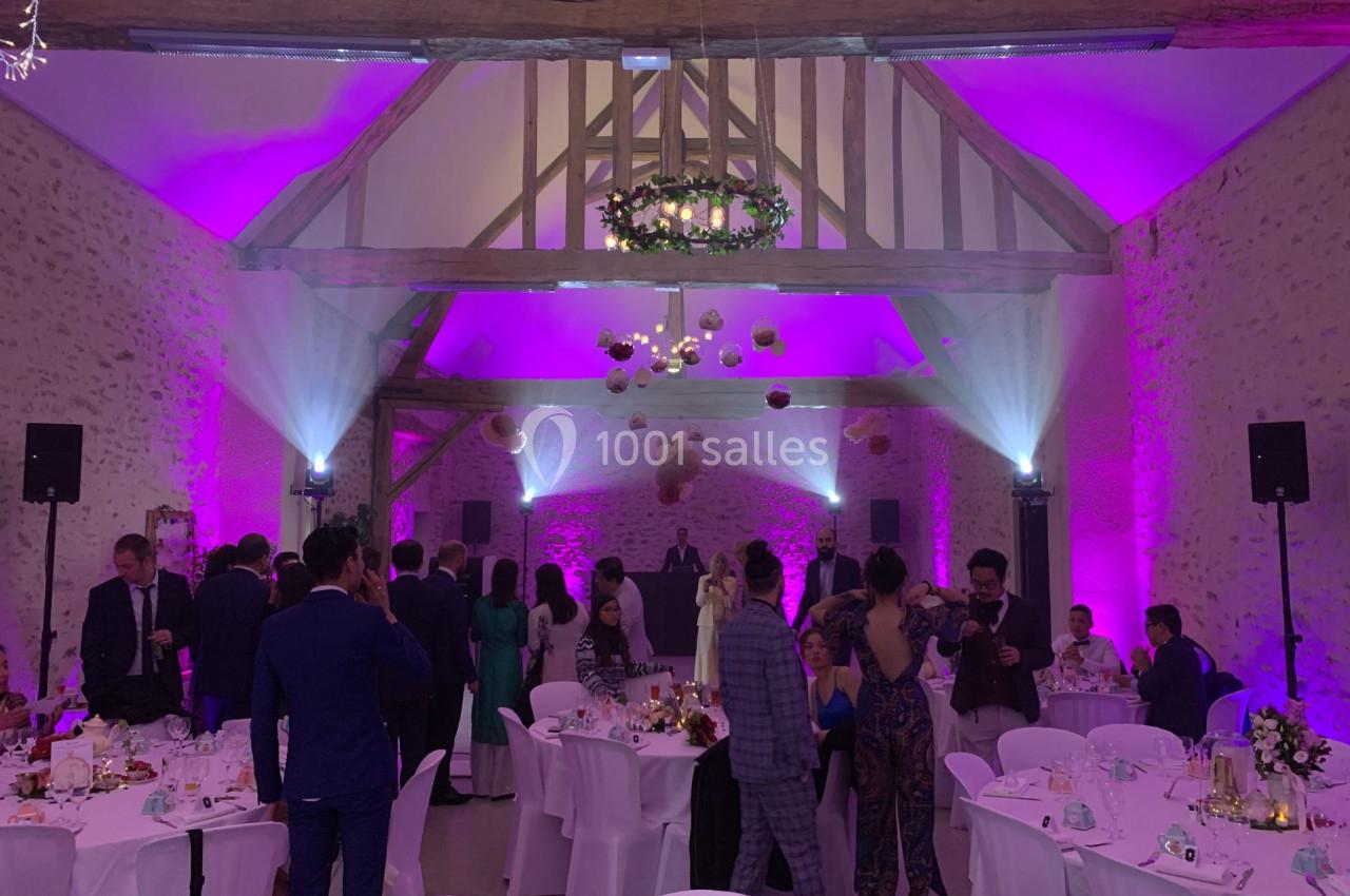 Salle de réception décorée avec des lumières violettes, des invités debout et assis autour de tables dressées.