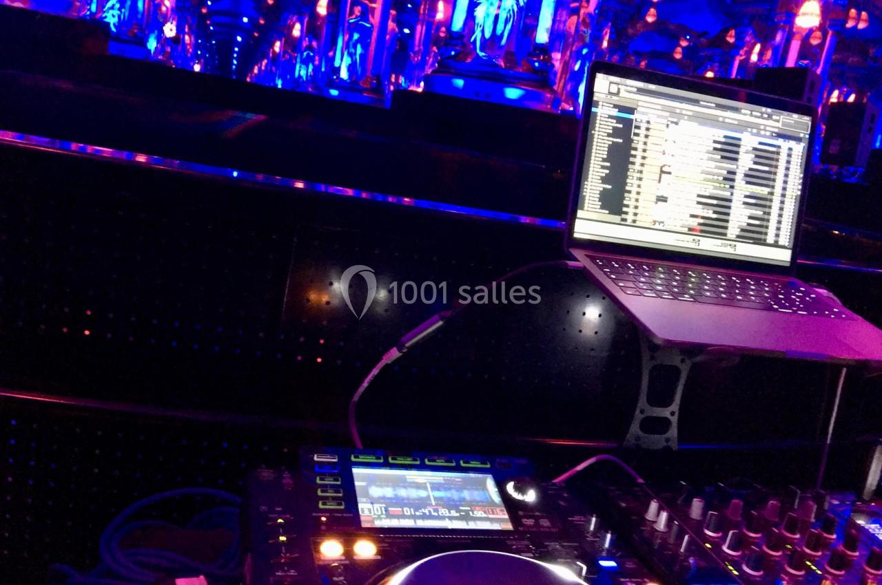 Console de mixage et ordinateur portable affichant une playlist, dans un environnement éclairé par des lumières bleues.