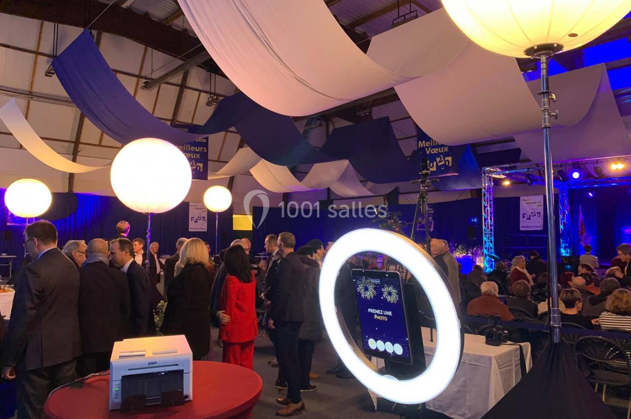 Salle décorée pour un événement avec des invités, des éclairages colorés et une borne photo équipée d'un anneau lumineux.