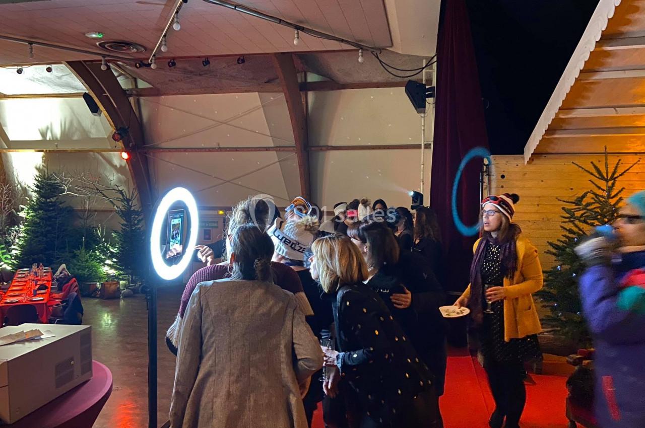 Groupe de personnes rassemblées autour d'une borne photo lumineuse dans une salle décorée avec des sapins.